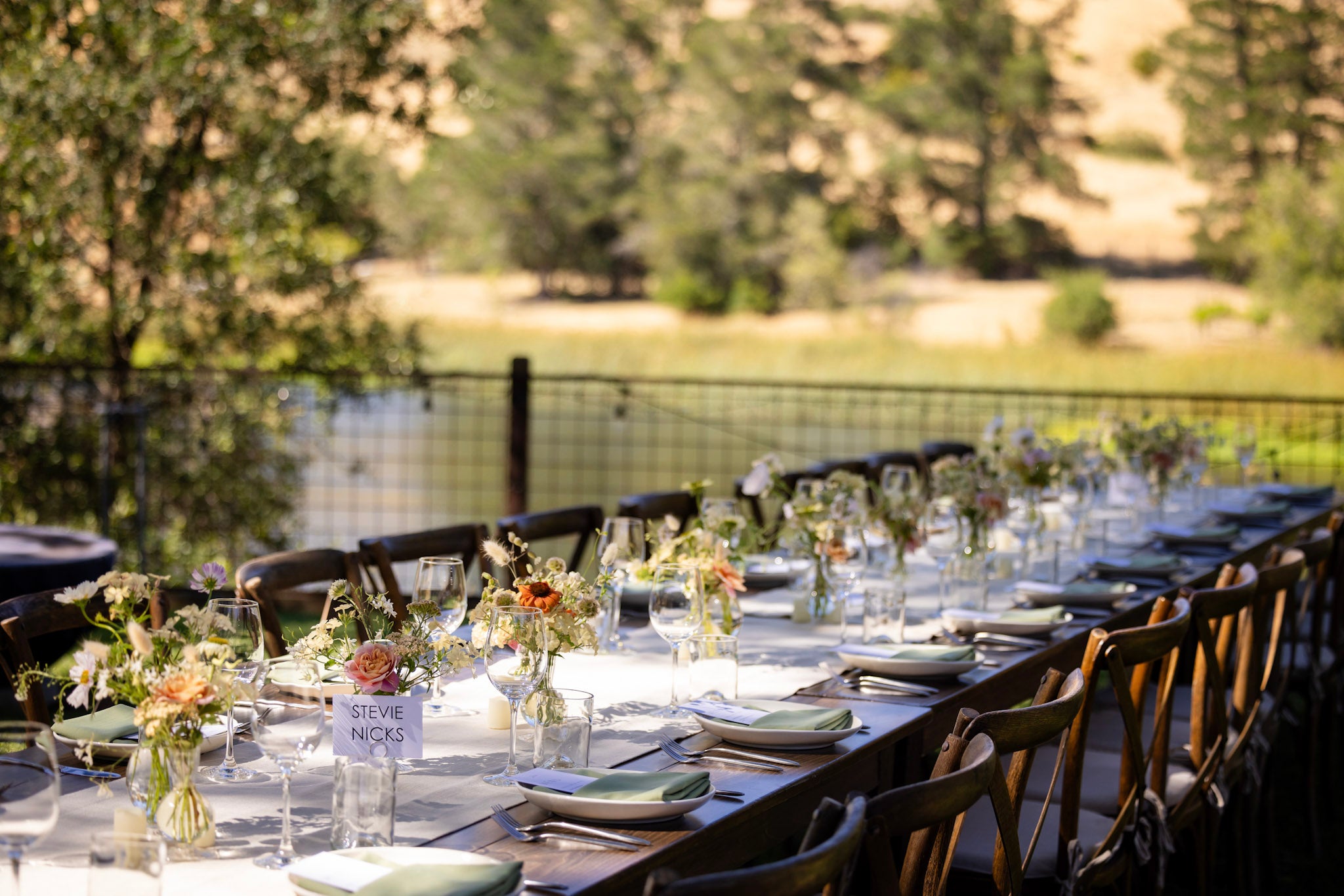 Long table with floral bud vase arrangements set for an outdoor wedding on the Russian River in Sonoma County.